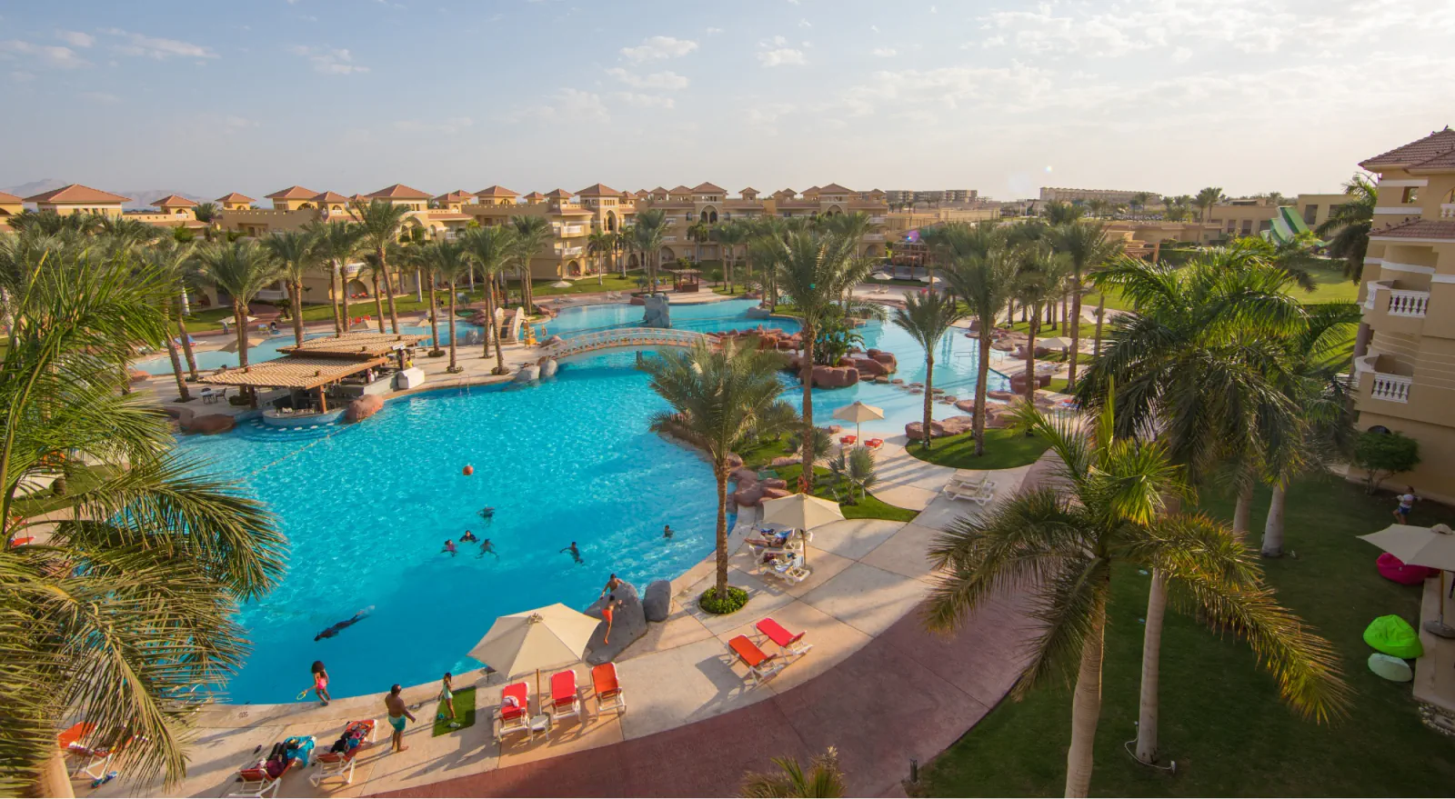 Palm-lined resort pool and surrounding villas viewed from above at golden hour