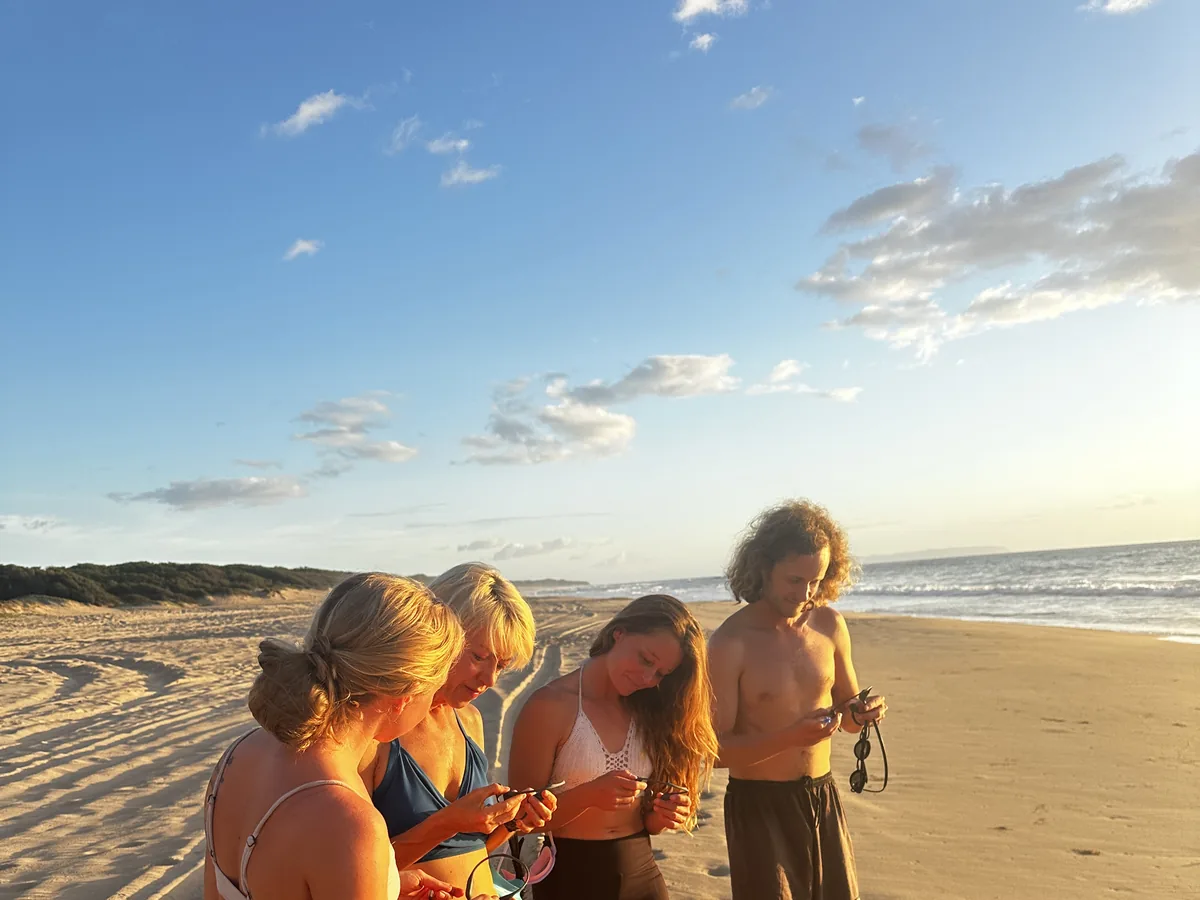 A group of friends fitting SubMergence headsets together on a Kaua'i beach before a sunset swim