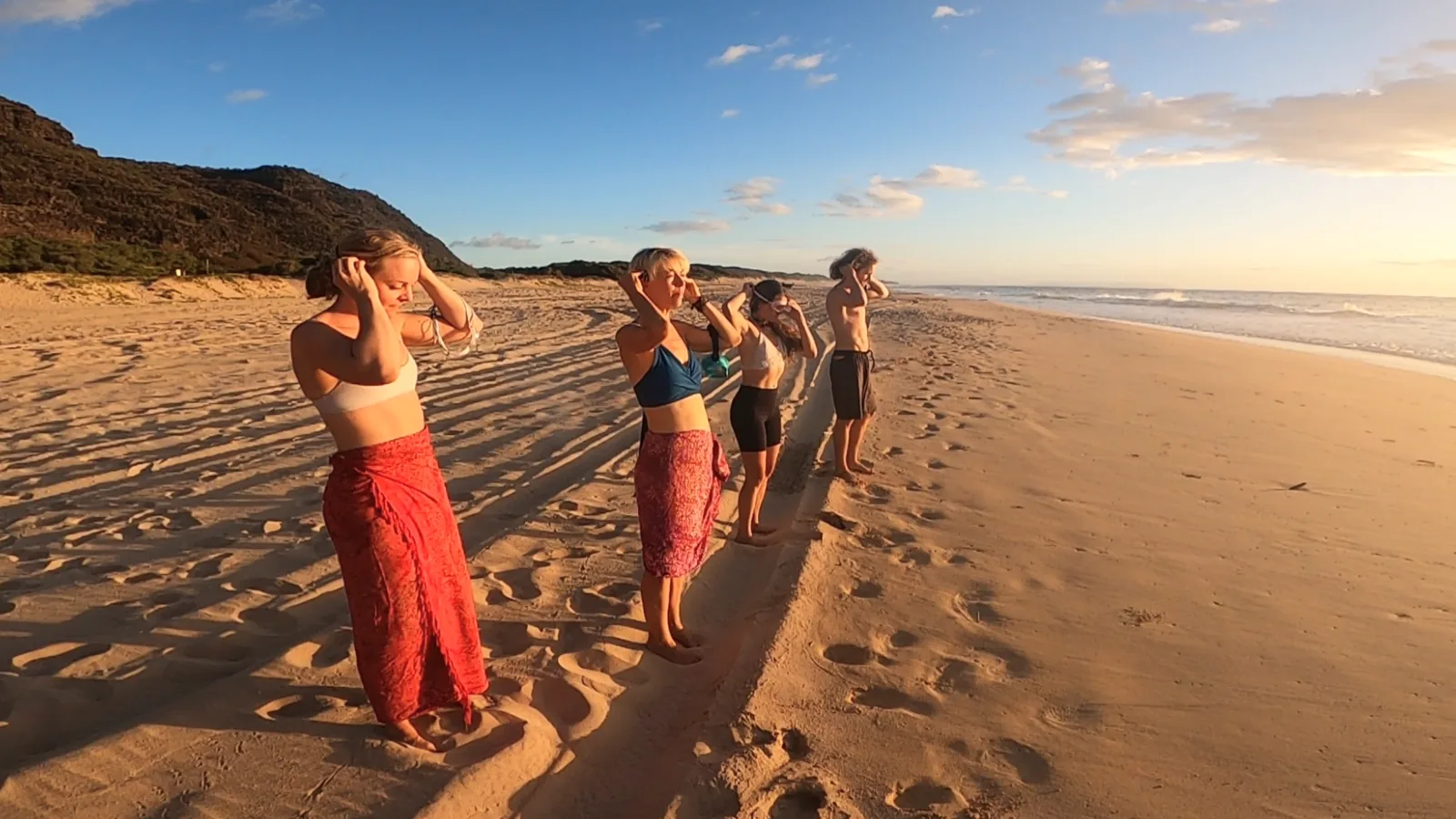 Four friends putting on SubMergence headsets along the shoreline as the sun sets over Kaua'i