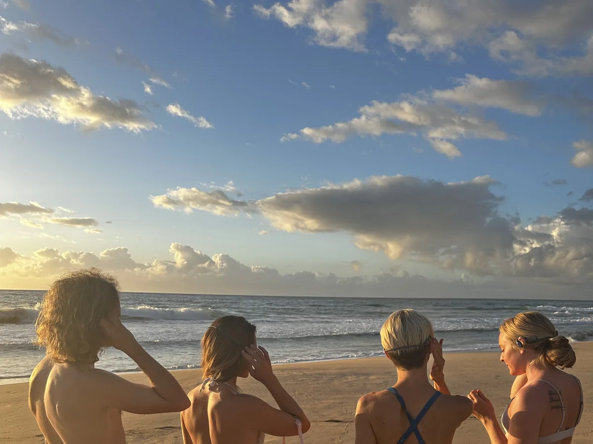 Four friends standing at the shoreline in SubMergence headsets, watching the sunset over the ocean on Kaua'i