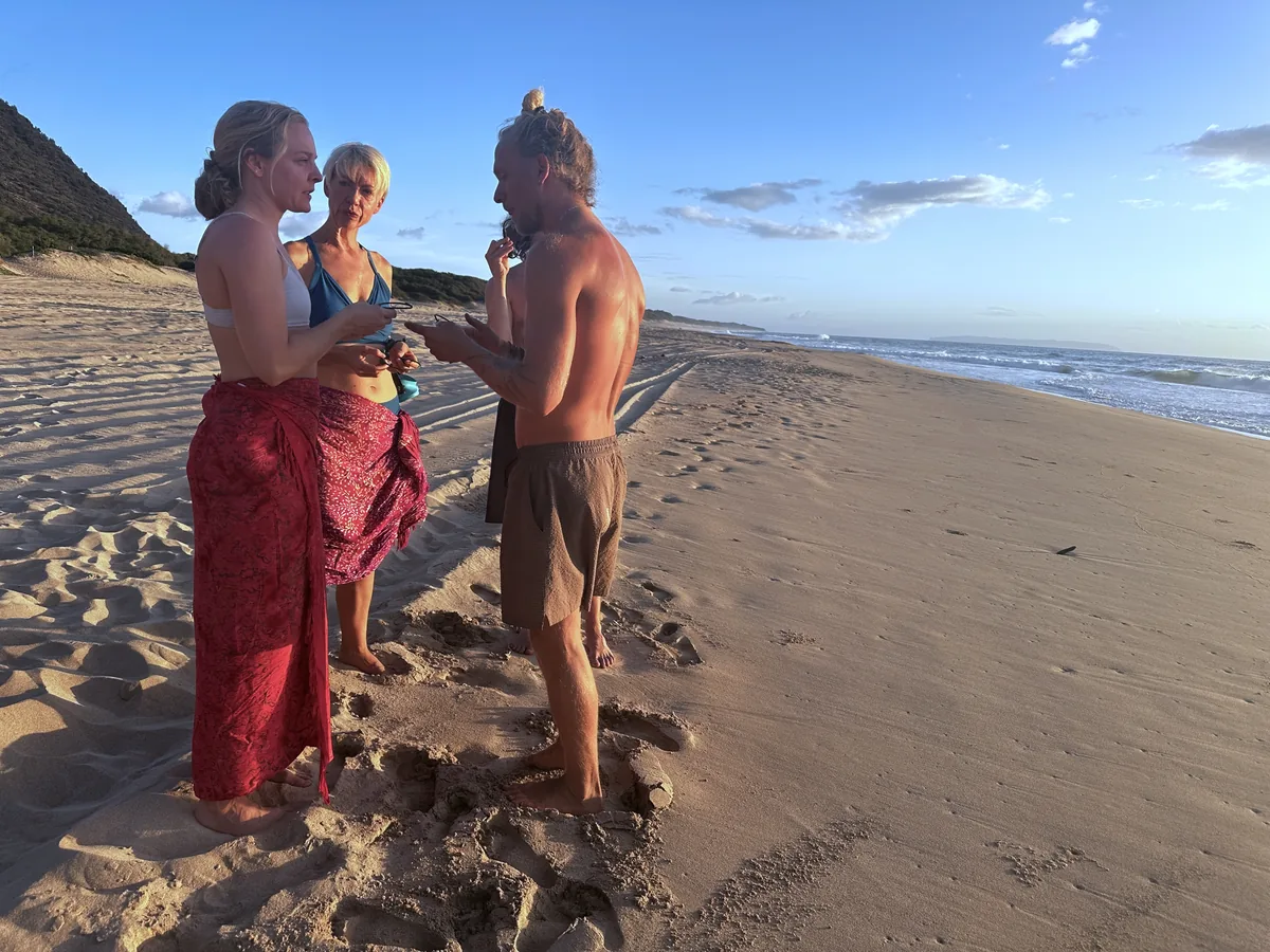 SubMergence founder Alex helping two friends fit bone-conduction headsets before an ocean swim at golden hour