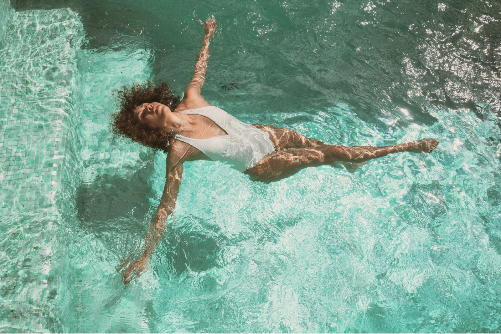 A person relaxing in a bright turquoise resort pool viewed from above